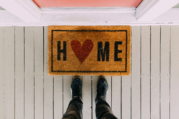 Doormat on a porch that says "HOME" with a heart shape in place of the O